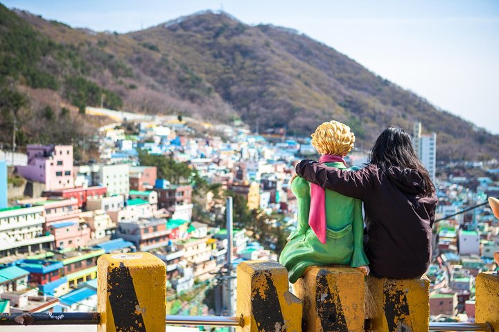 Colorful homes cascade down the hillside with friends enjoying the serene view of Busan’s remarkable blend of nature and art. A perfect escape into local culture and stunning landscapes awaits.